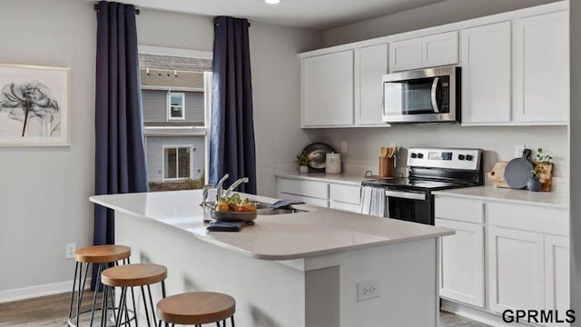 kitchen featuring an island with sink, sink, a breakfast bar area, white cabinets, and stainless steel appliances