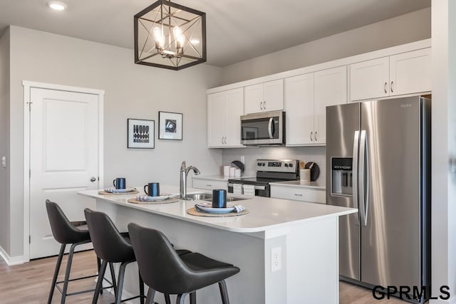 kitchen featuring pendant lighting, stainless steel appliances, an island with sink, and white cabinets