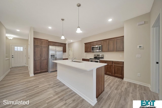 kitchen with light wood-type flooring, appliances with stainless steel finishes, sink, pendant lighting, and a center island with sink