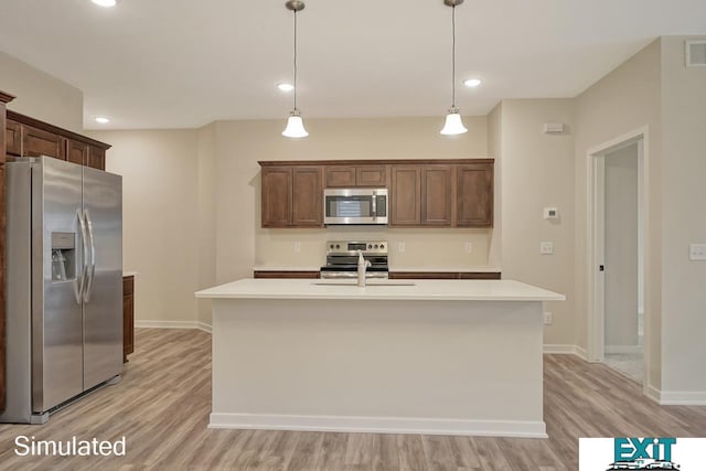 kitchen with an island with sink, hanging light fixtures, stainless steel appliances, sink, and light wood-type flooring