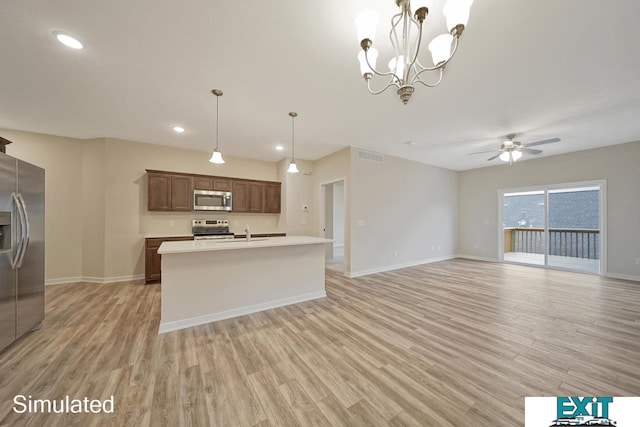 kitchen featuring light wood-type flooring, ceiling fan with notable chandelier, stainless steel appliances, hanging light fixtures, and a center island with sink