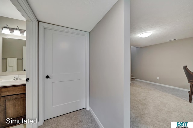 corridor featuring light colored carpet, a textured ceiling, and sink