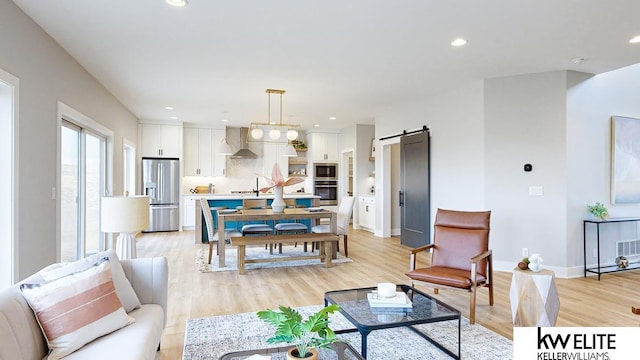 living area featuring light wood finished floors, a barn door, baseboards, and recessed lighting