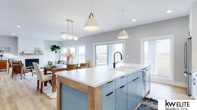 kitchen featuring a large fireplace, stainless steel appliances, a sink, light wood-style floors, and decorative light fixtures