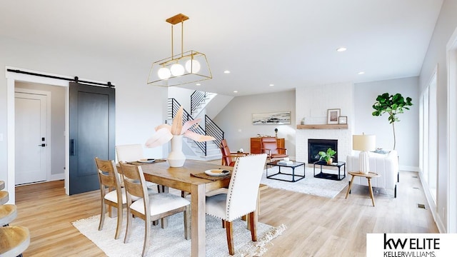 dining room with a fireplace, light wood finished floors, recessed lighting, stairway, and a barn door