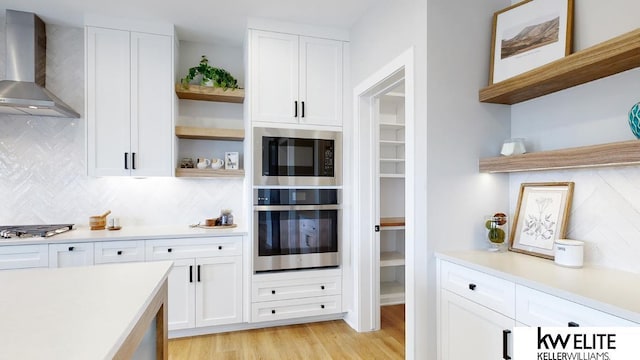 kitchen featuring white cabinets, light countertops, appliances with stainless steel finishes, wall chimney exhaust hood, and open shelves