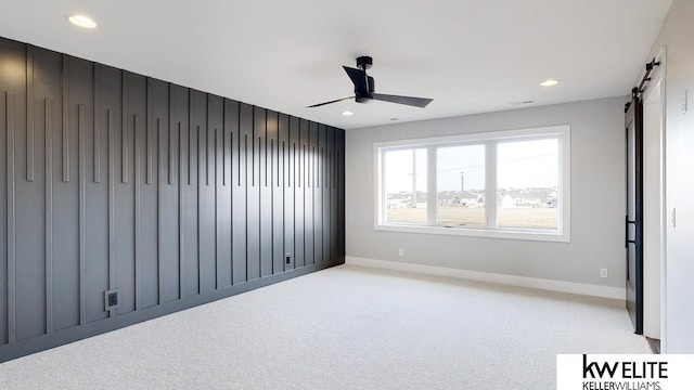 empty room with ceiling fan, a barn door, recessed lighting, light carpet, and baseboards