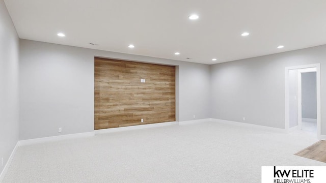 carpeted empty room with wooden walls, baseboards, and recessed lighting