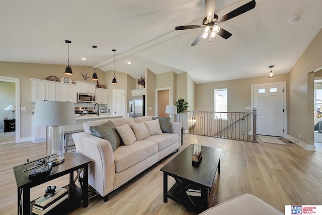 living room featuring ceiling fan, sink, light wood-type flooring, and vaulted ceiling