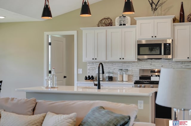 kitchen featuring appliances with stainless steel finishes, decorative light fixtures, an island with sink, and white cabinets