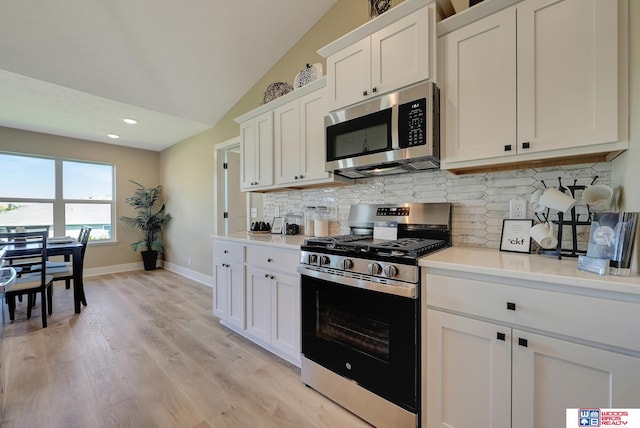 kitchen featuring appliances with stainless steel finishes, white cabinetry, backsplash, light wood-type flooring, and lofted ceiling