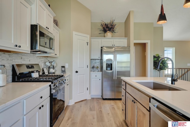 kitchen featuring appliances with stainless steel finishes, light hardwood / wood-style floors, white cabinetry, pendant lighting, and sink