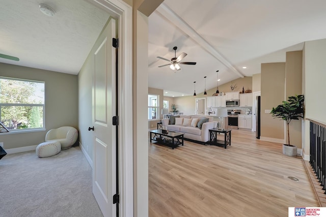 living room featuring a textured ceiling, light hardwood / wood-style floors, sink, vaulted ceiling with beams, and ceiling fan