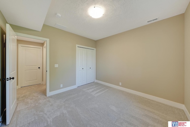 unfurnished bedroom featuring a textured ceiling, light colored carpet, and a closet