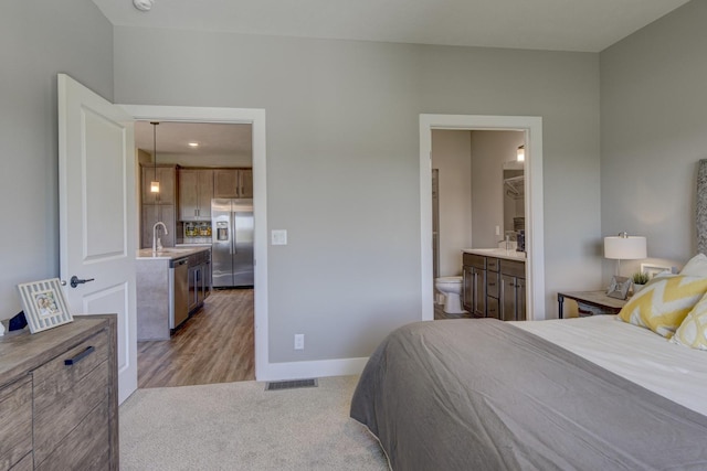 bedroom featuring visible vents, baseboards, ensuite bathroom, stainless steel refrigerator with ice dispenser, and light colored carpet