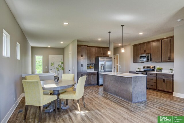 kitchen featuring a sink, an island with sink, wood finished floors, and stainless steel appliances