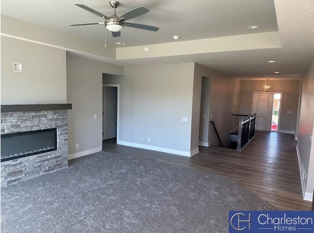 unfurnished living room with a fireplace, ceiling fan, a raised ceiling, and dark wood-type flooring