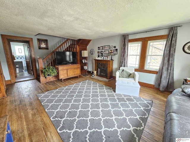 living room featuring baseboards, wood-type flooring, stairway, a textured ceiling, and a fireplace