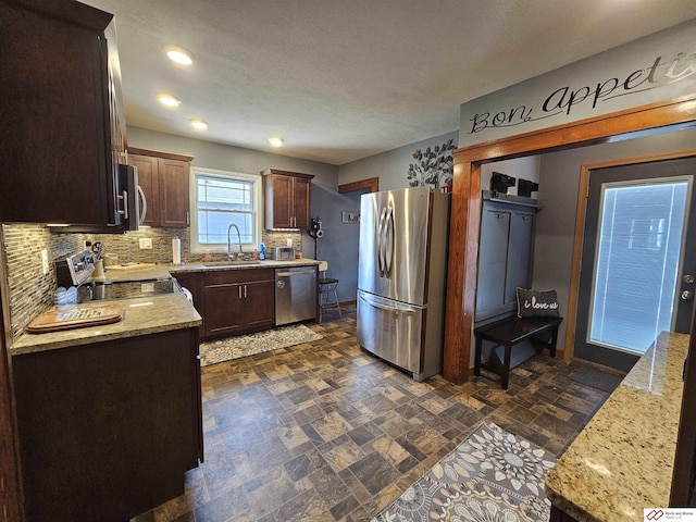 kitchen featuring a sink, baseboards, appliances with stainless steel finishes, stone finish flooring, and tasteful backsplash