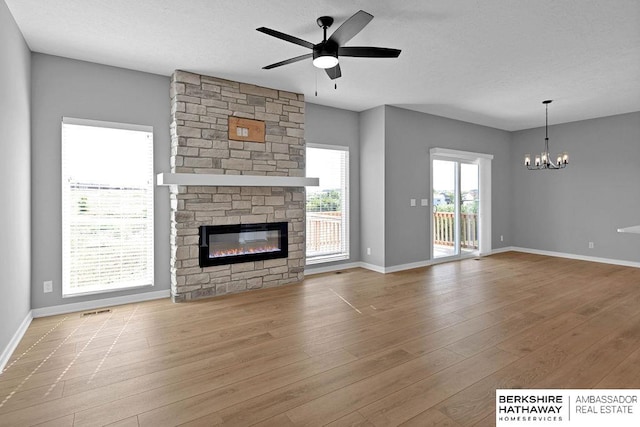 unfurnished living room with light hardwood / wood-style flooring, ceiling fan with notable chandelier, and a stone fireplace