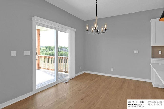 unfurnished dining area with an inviting chandelier and light hardwood / wood-style flooring