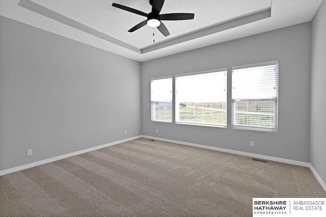 carpeted spare room with ceiling fan and a raised ceiling