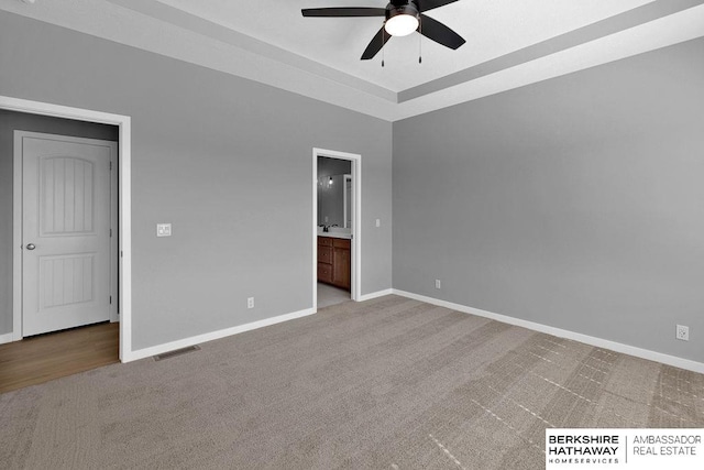 unfurnished bedroom with ceiling fan, carpet, a tray ceiling, and ensuite bath