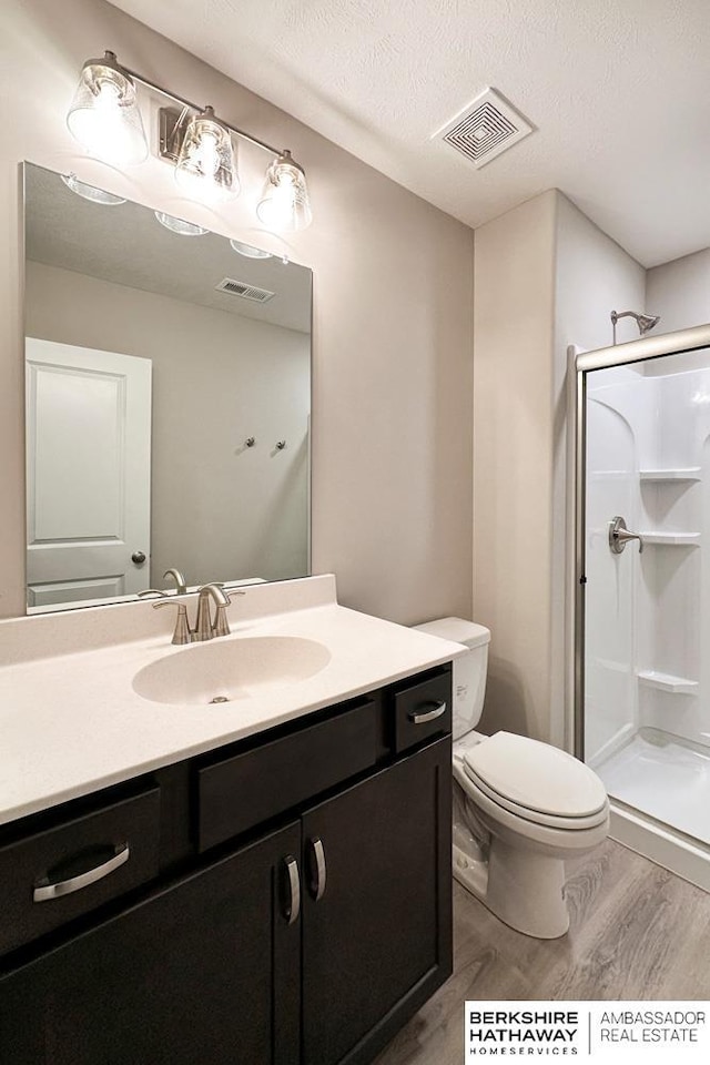 bathroom featuring toilet, vanity, hardwood / wood-style floors, a textured ceiling, and a shower with door