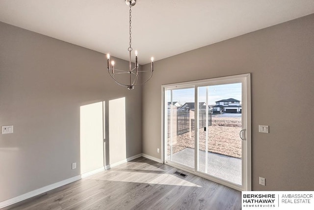 unfurnished dining area with an inviting chandelier and hardwood / wood-style flooring