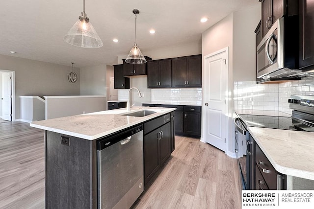 kitchen with an island with sink, stainless steel appliances, pendant lighting, light hardwood / wood-style flooring, and sink