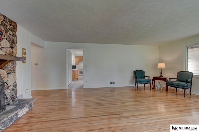 living area featuring a stone fireplace, a textured ceiling, and light hardwood / wood-style flooring