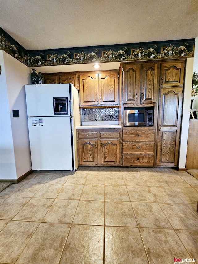 kitchen featuring stainless steel microwave, white fridge with ice dispenser, a textured ceiling, and light tile patterned flooring