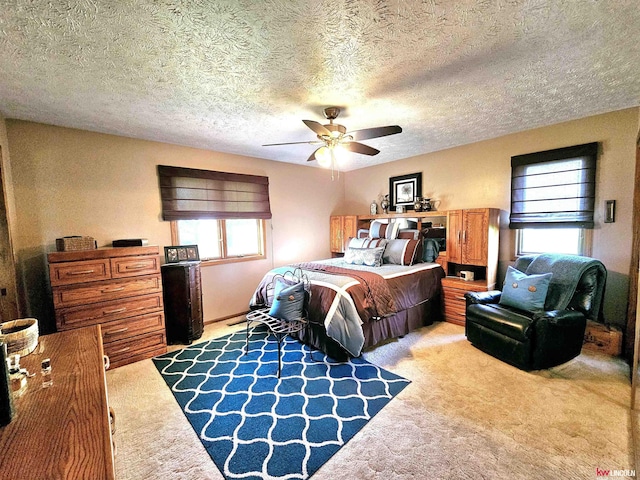 bedroom with ceiling fan, light colored carpet, and a textured ceiling