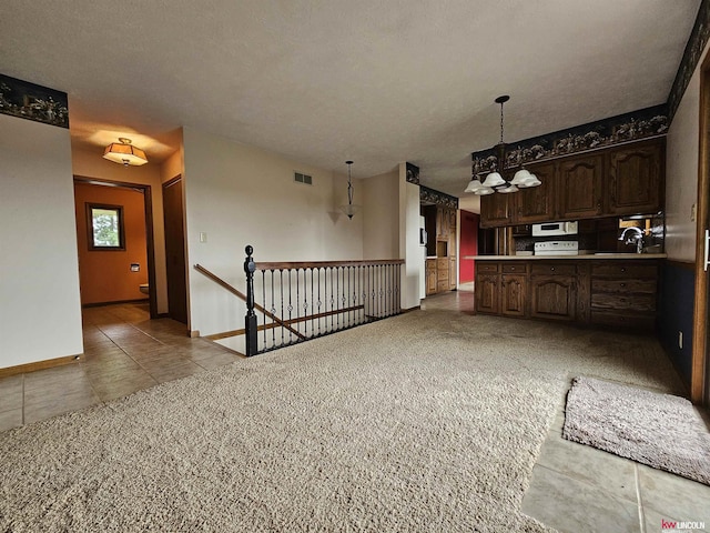 kitchen with hanging light fixtures, light colored carpet, a textured ceiling, and dark brown cabinetry