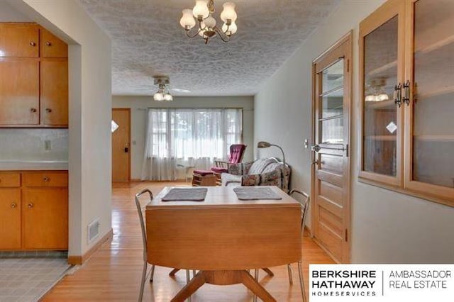 dining area with an inviting chandelier, a textured ceiling, and light wood-type flooring