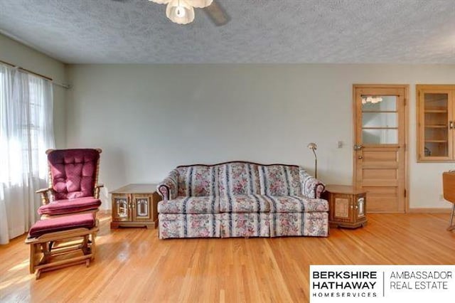 living room featuring ceiling fan, a textured ceiling, and light wood-type flooring