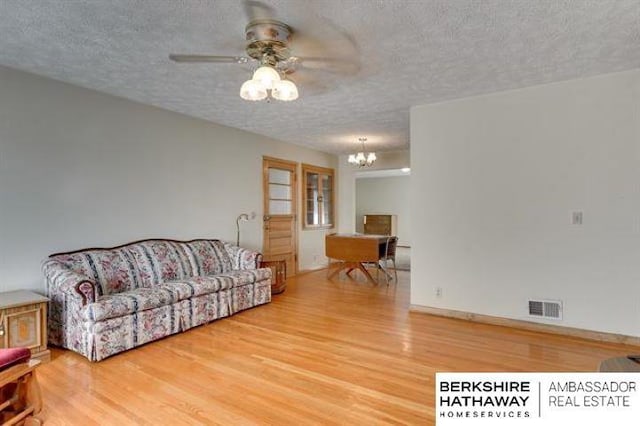 living room featuring wood-type flooring, ceiling fan with notable chandelier, and a textured ceiling