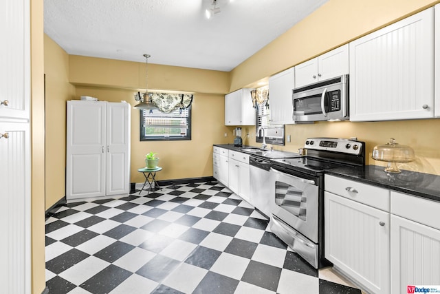 kitchen featuring appliances with stainless steel finishes, decorative light fixtures, white cabinetry, and dark tile patterned flooring