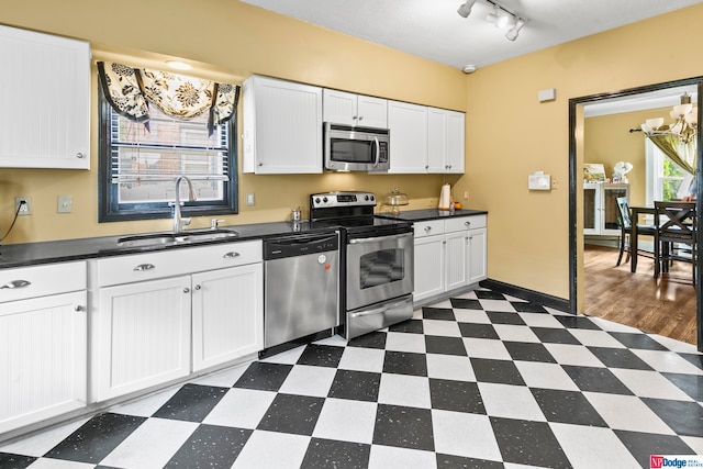 kitchen featuring appliances with stainless steel finishes, white cabinets, sink, rail lighting, and dark hardwood / wood-style flooring