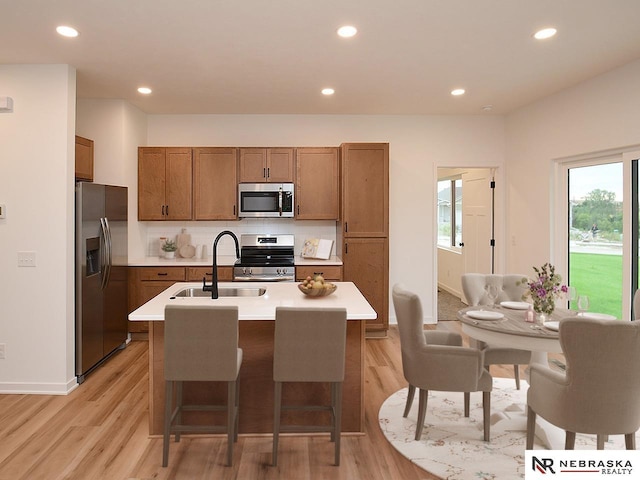 kitchen with an island with sink, stainless steel appliances, sink, and light hardwood / wood-style flooring