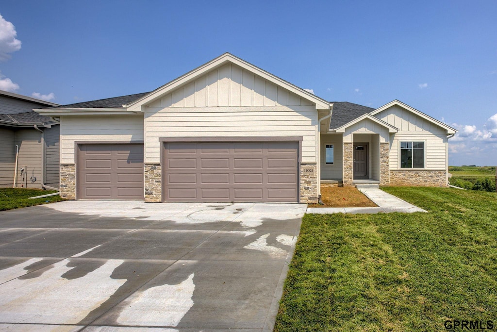 craftsman-style house featuring a garage, stone siding, concrete driveway, board and batten siding, and a front yard