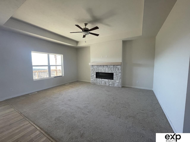 unfurnished living room featuring a tray ceiling, a fireplace, visible vents, a ceiling fan, and baseboards