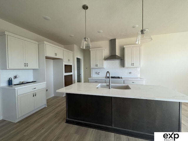 kitchen with a kitchen island with sink, white cabinets, wall chimney range hood, light stone countertops, and light wood-type flooring