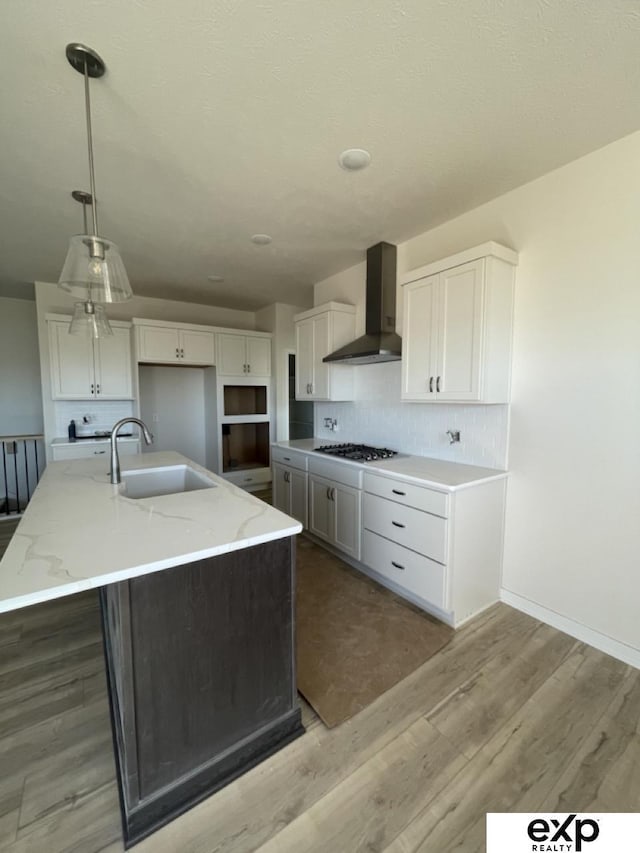 kitchen with light stone counters, tasteful backsplash, white cabinets, a sink, and wall chimney exhaust hood