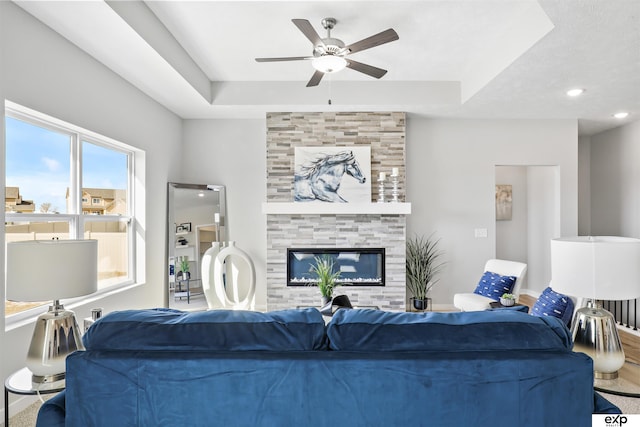 living room featuring a large fireplace, ceiling fan, and a raised ceiling