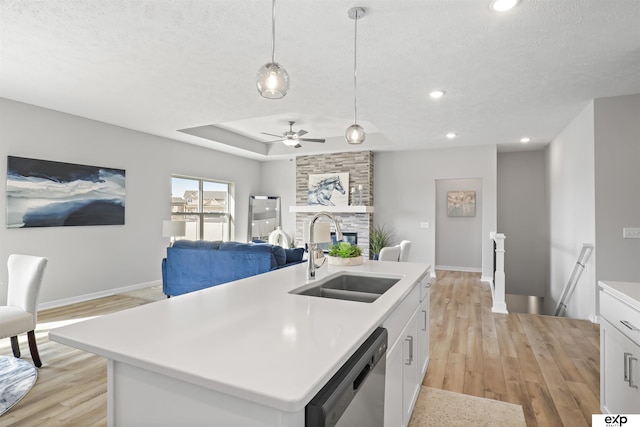 kitchen featuring light hardwood / wood-style flooring, a stone fireplace, sink, stainless steel dishwasher, and a kitchen island with sink