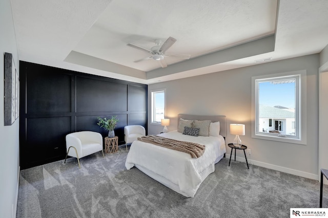 carpeted bedroom with a raised ceiling and ceiling fan