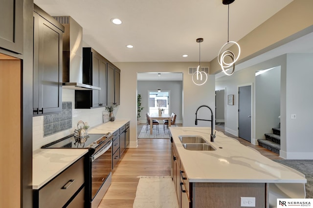 kitchen with light stone counters, decorative light fixtures, light wood-type flooring, electric range, and wall chimney exhaust hood