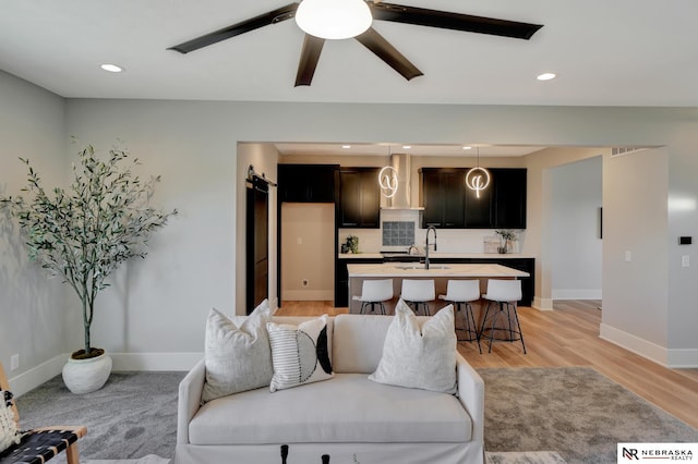 living room with light hardwood / wood-style floors, sink, a barn door, and ceiling fan