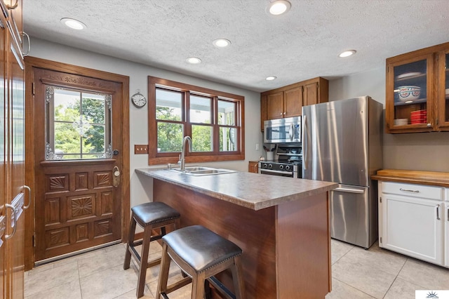 kitchen featuring a breakfast bar area, light tile patterned floors, a textured ceiling, appliances with stainless steel finishes, and sink